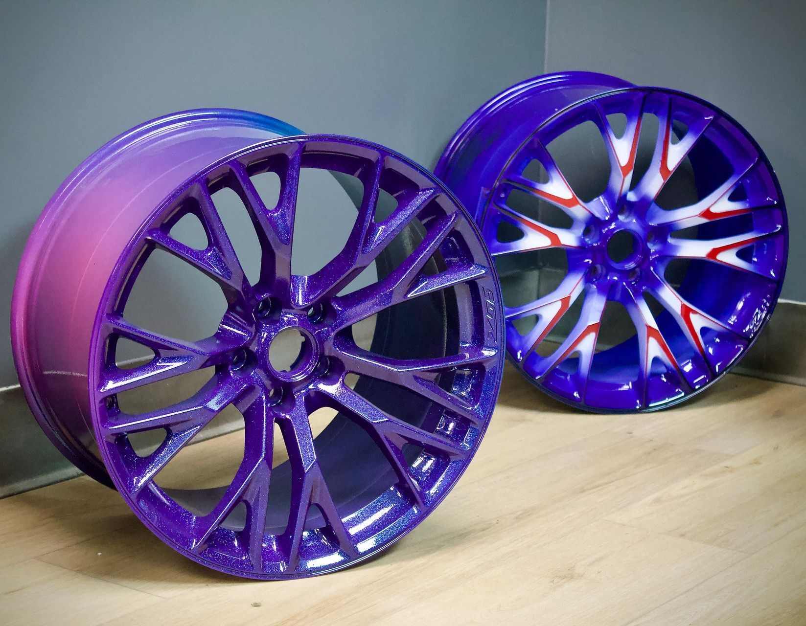 Two purple alloy car rims, one with a pink gradient and one with white accents, on a wooden surface