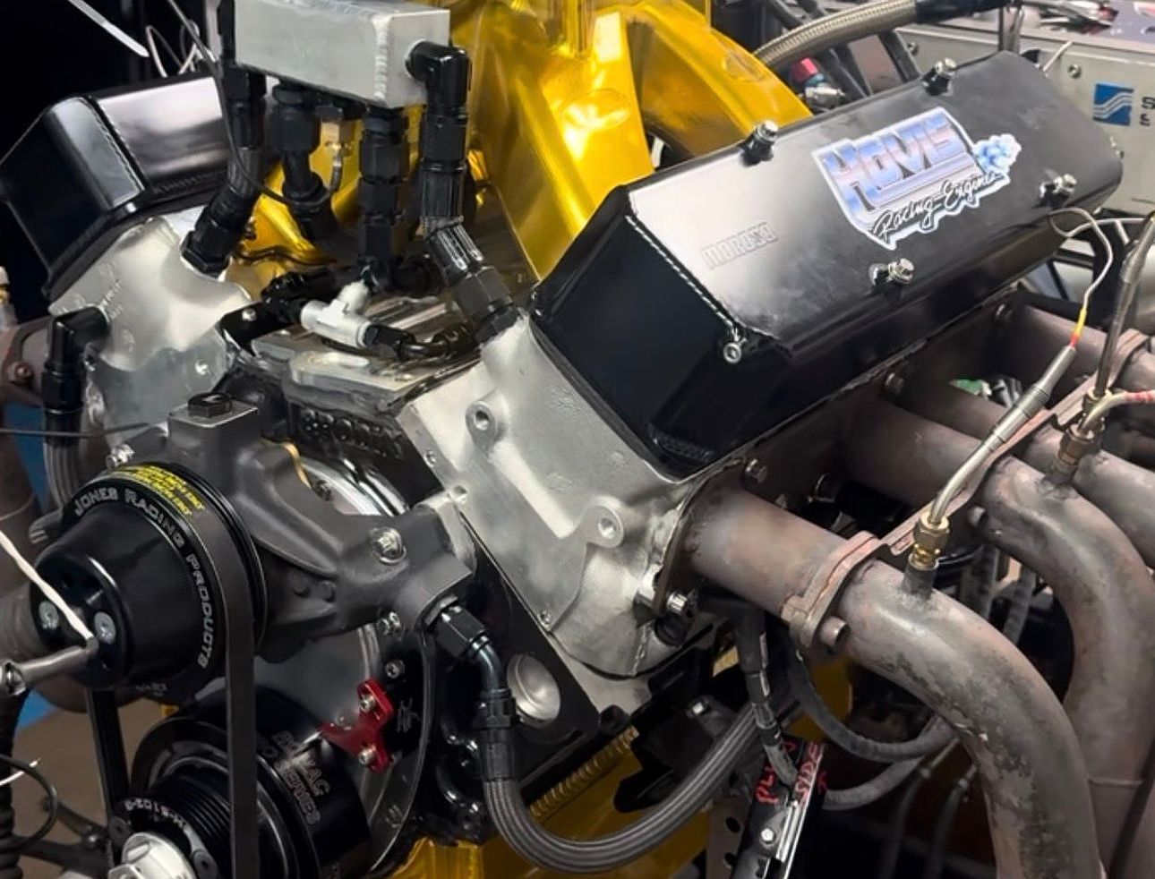Close-up of a car engine bay with a yellow engine block and chrome exhaust headers.