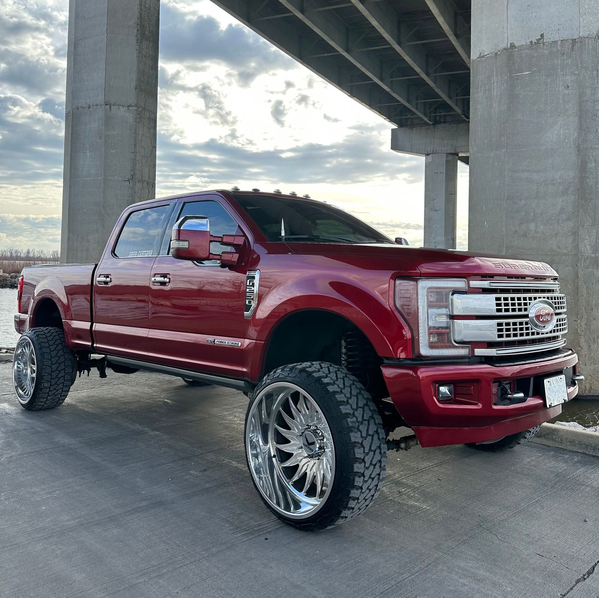Red lifted pickup truck with chrome wheels parked under an overpass at sunset