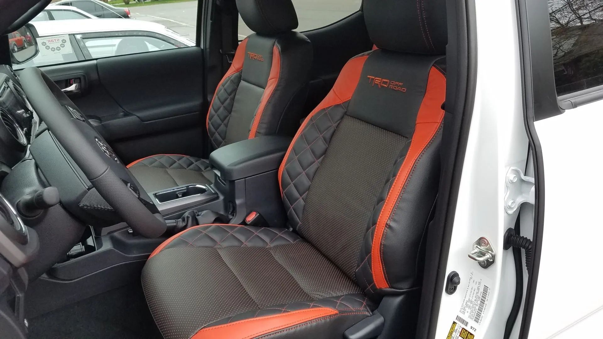 Car interior with black-and-orange sport seats and steering wheel visible, door open.