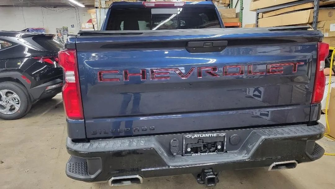 Rear view of a gray Chevrolet pickup truck in a garage, with tailgate and trailer hitch visible
