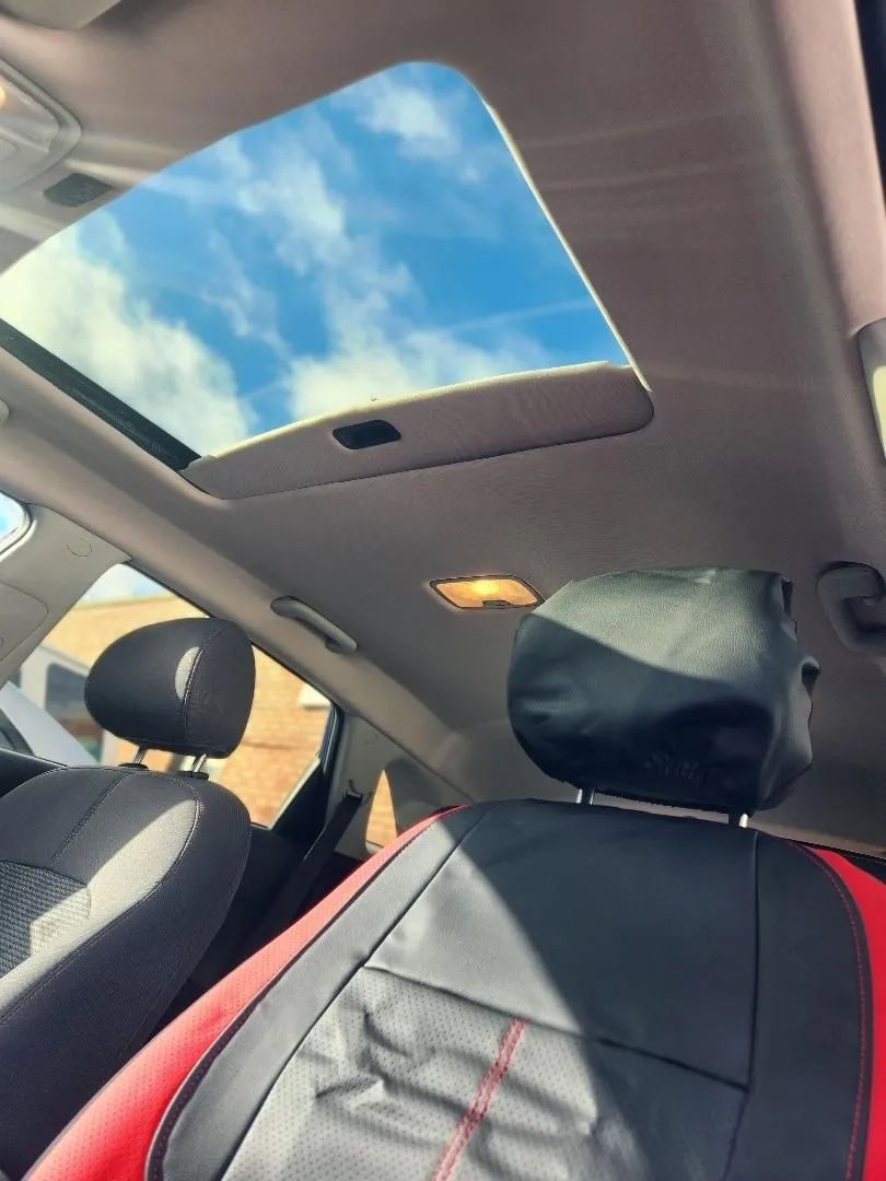 Car interior with front seats and open sunroof showing blue sky and clouds