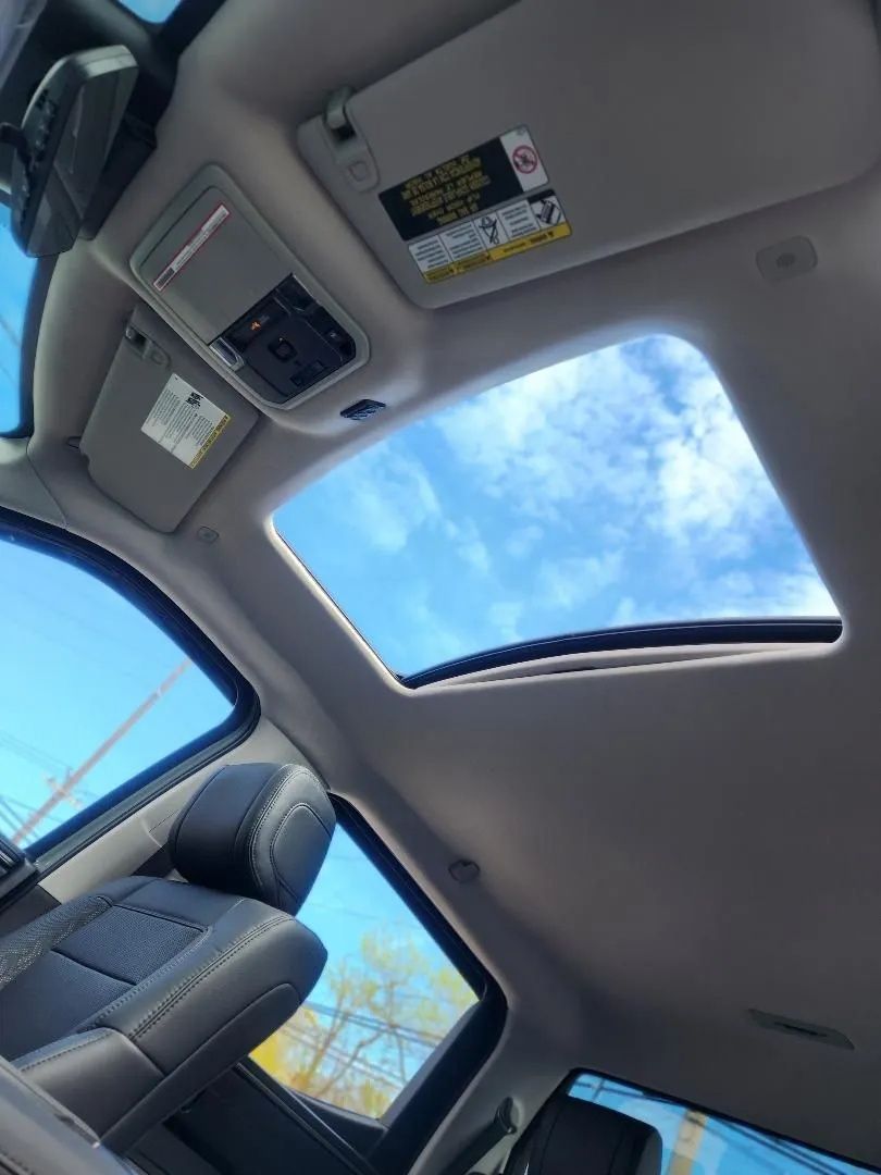 Car interior with open sunroof, blue sky visible, and a front seat with patterned upholstery