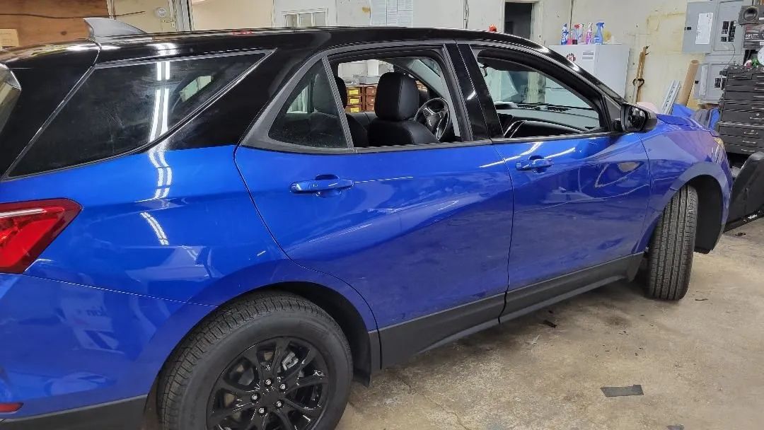 Blue SUV in a garage, side view, with black wheels and rear passenger door open.