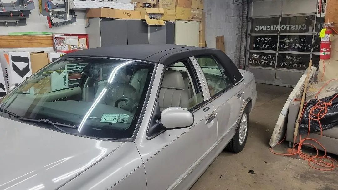 Silver sedan parked in a cluttered garage beside tools and equipment.