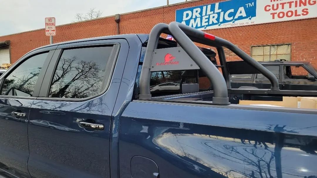 Blue pickup truck with a black roll bar parked in front of a Drill America sign