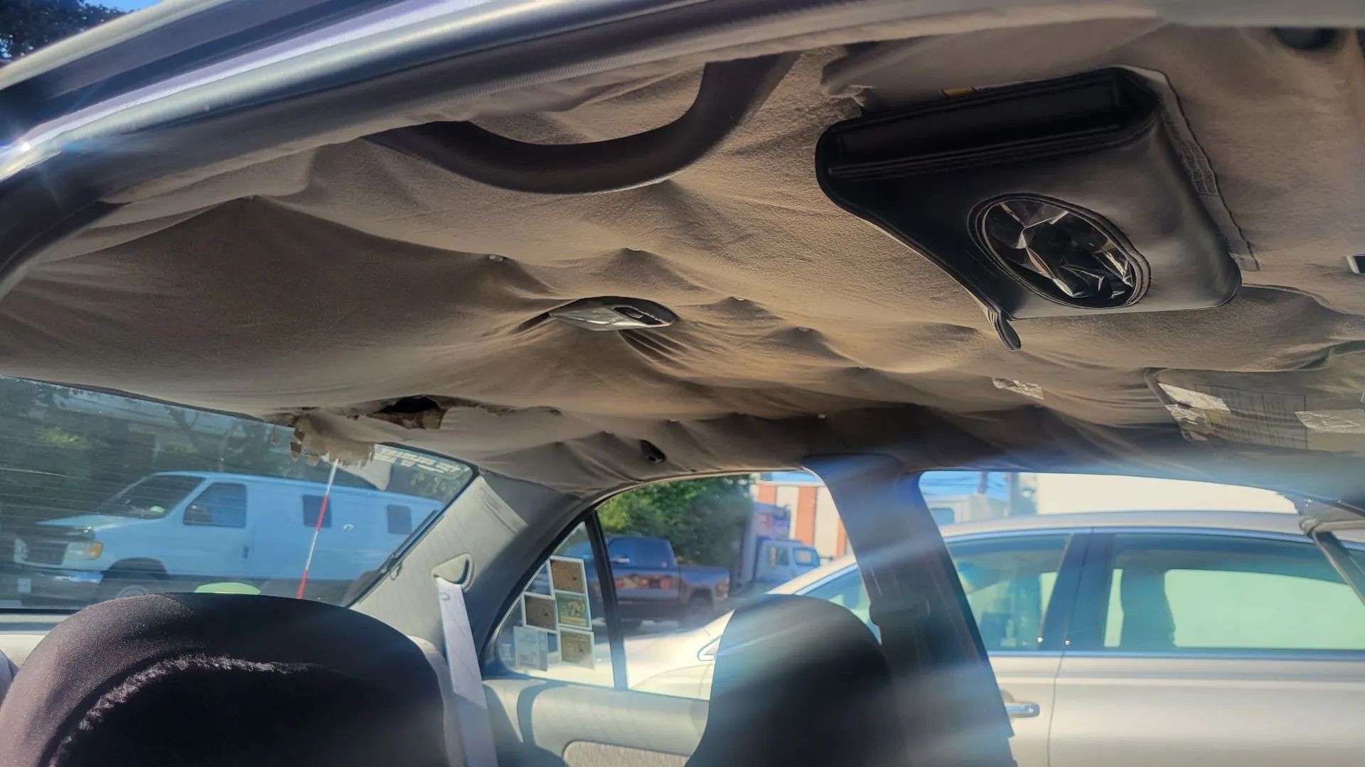 Car interior with the headliner sagging and hanging down above the front seats.