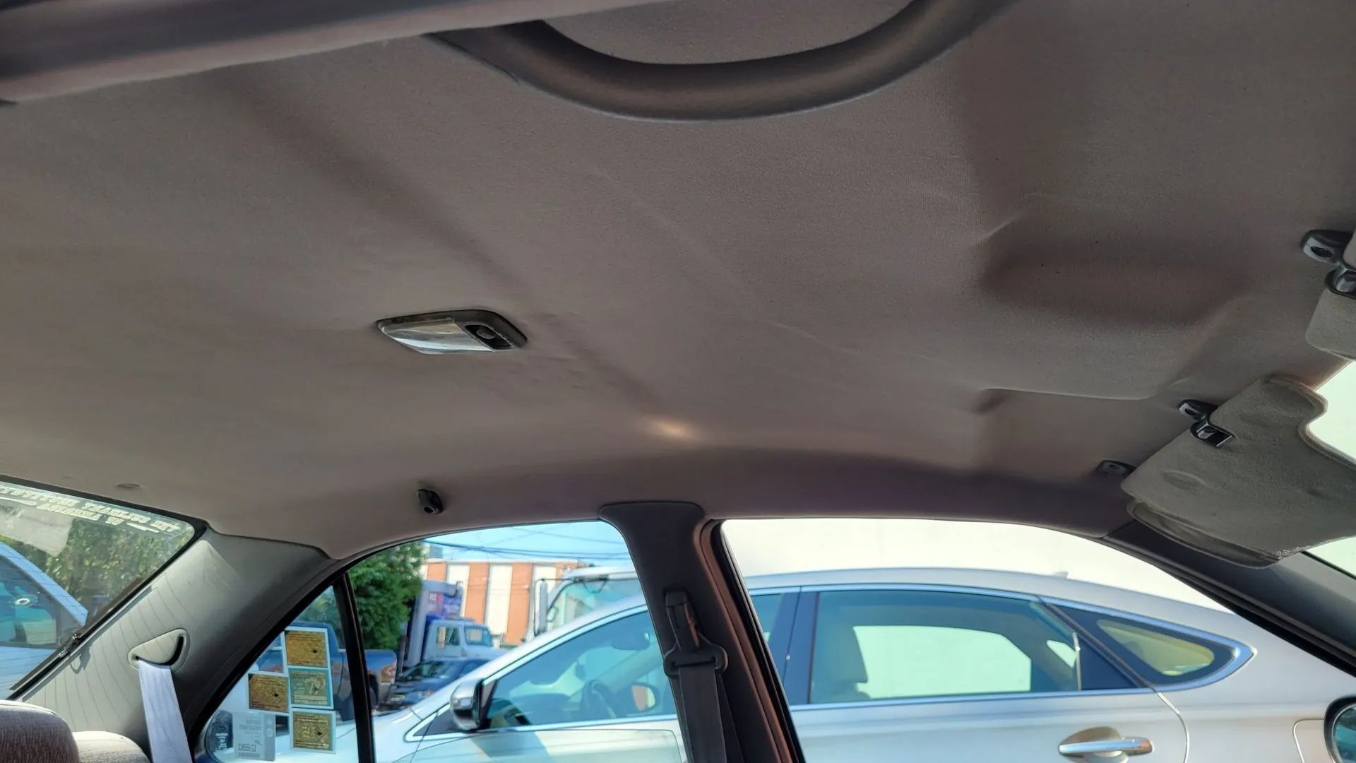 Car interior ceiling with exposed wiring and open panel, parked near other cars outdoors