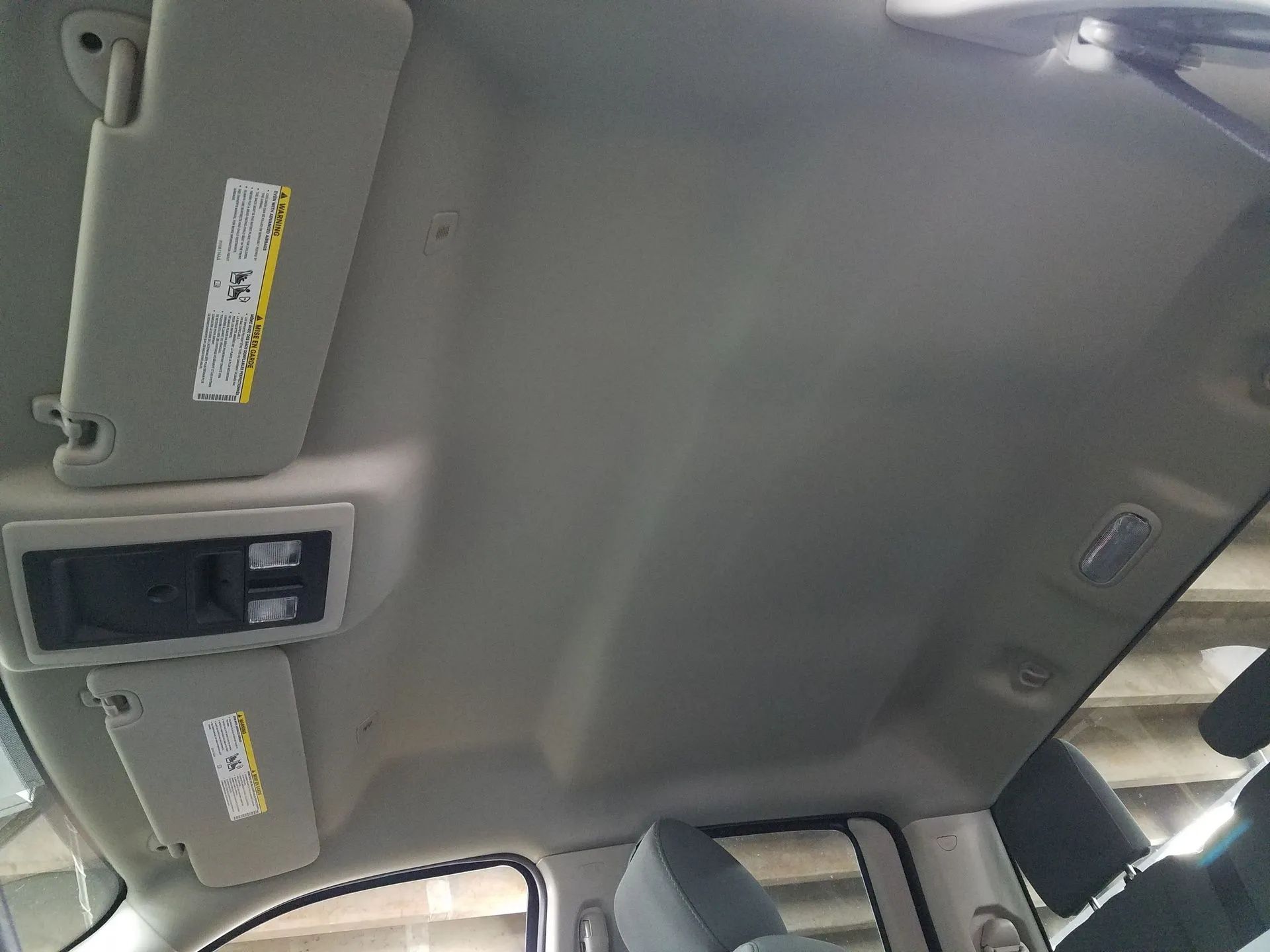 Car ceiling with sun visor, overhead console, and dome light; a seat and window are visible below