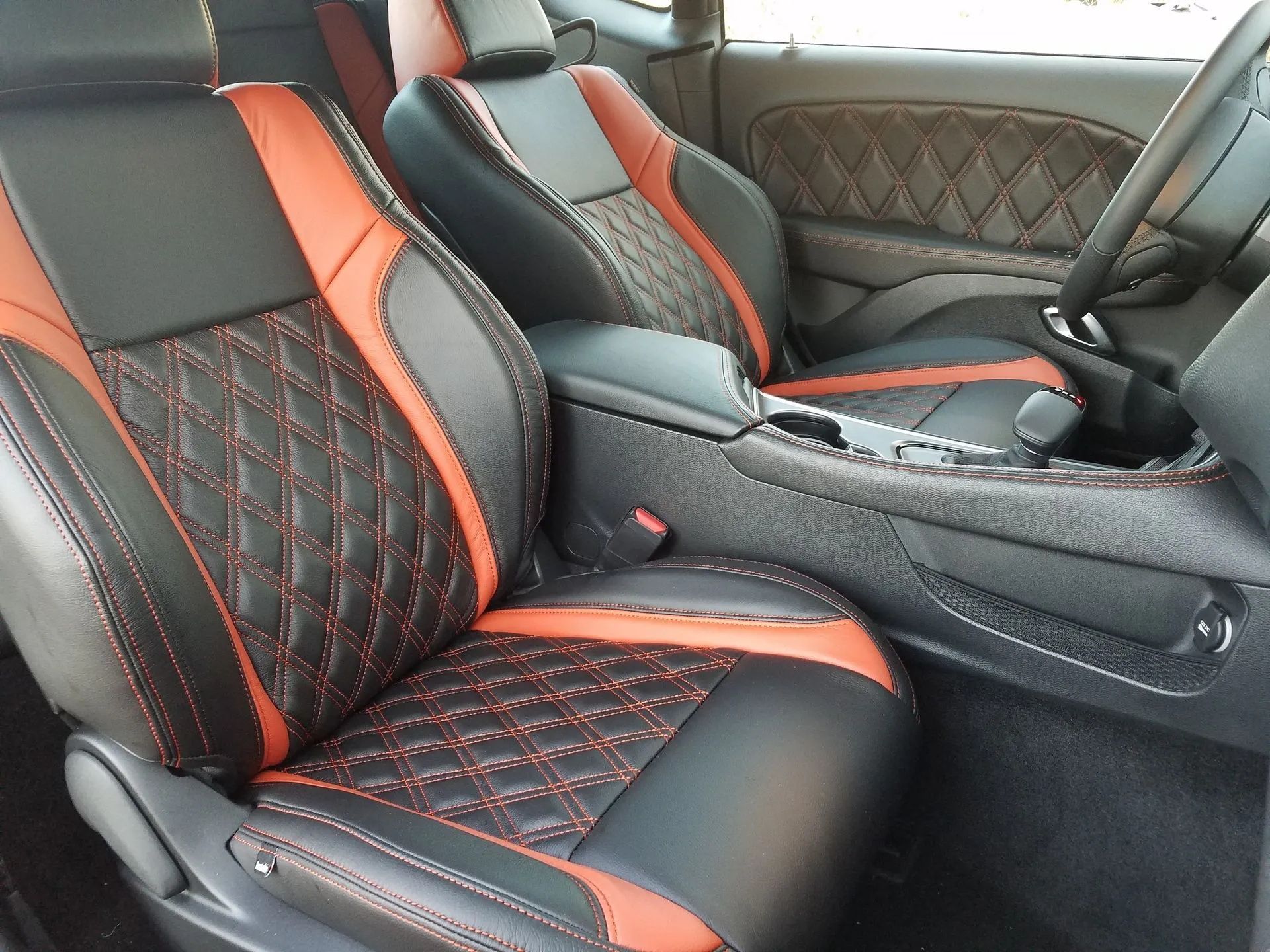 Custom black and orange car seats with diamond stitching inside a vehicle interior