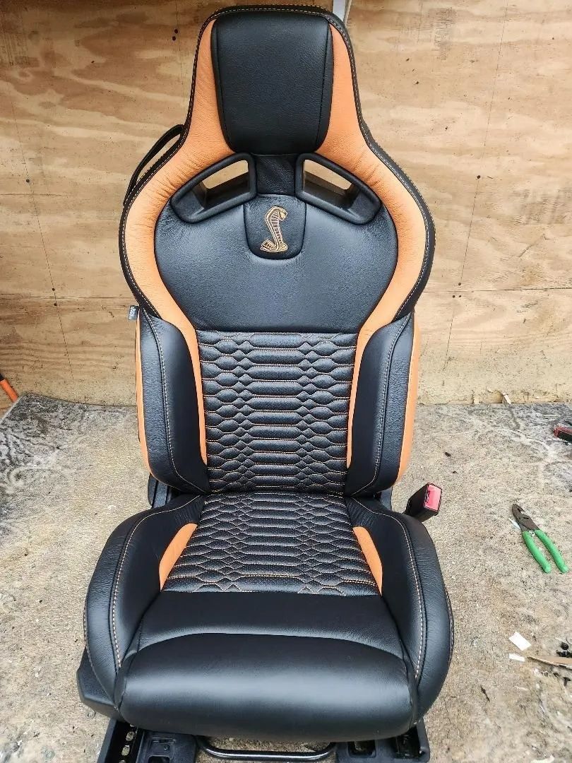 Black and tan racing-style car seat with padded headrest on a concrete floor