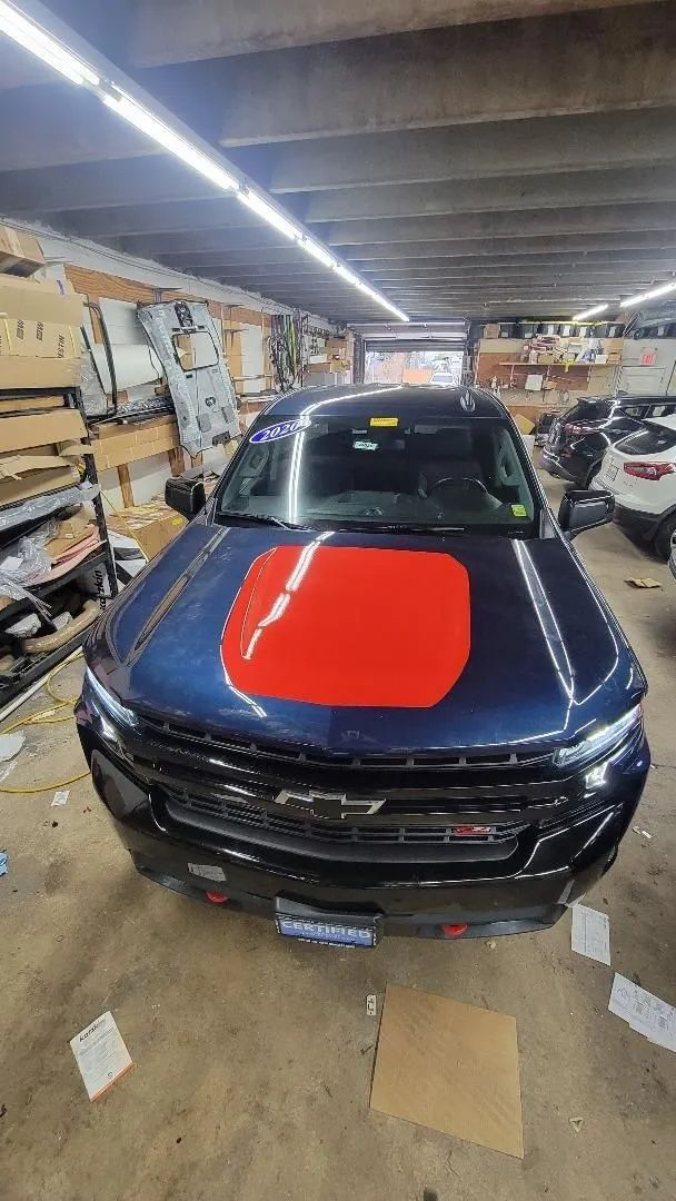 Blue car with a red hood decal in a cluttered garage or workshop.