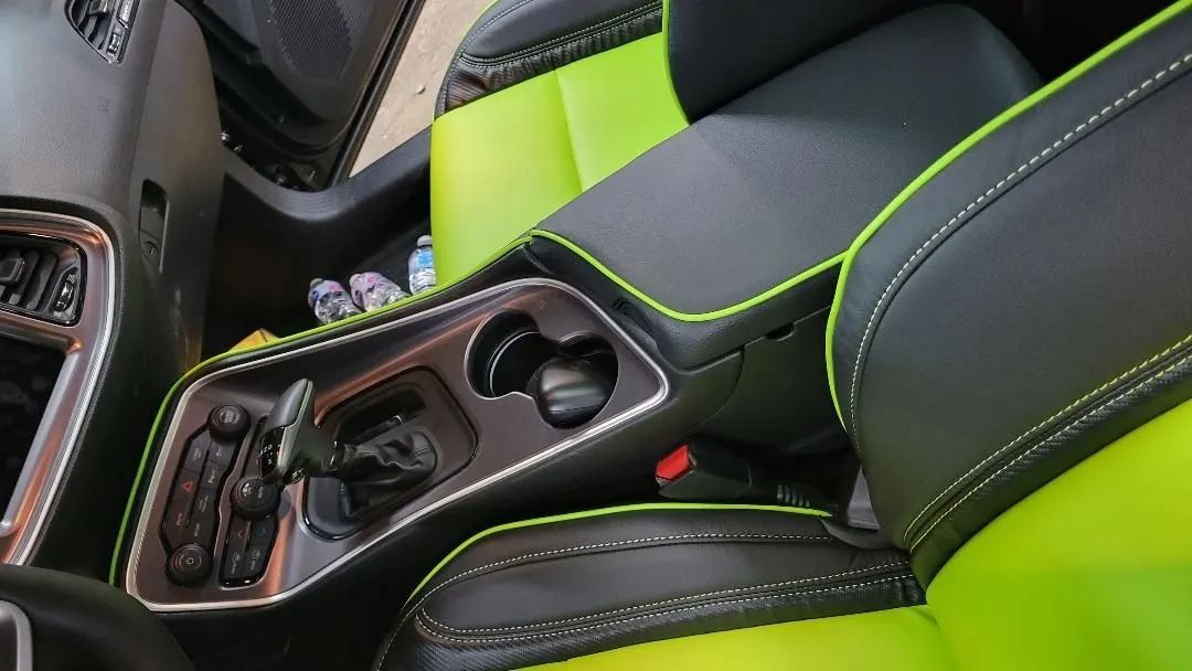 Car interior with black leather seats, lime green accents, and a center console with cup holders and controls