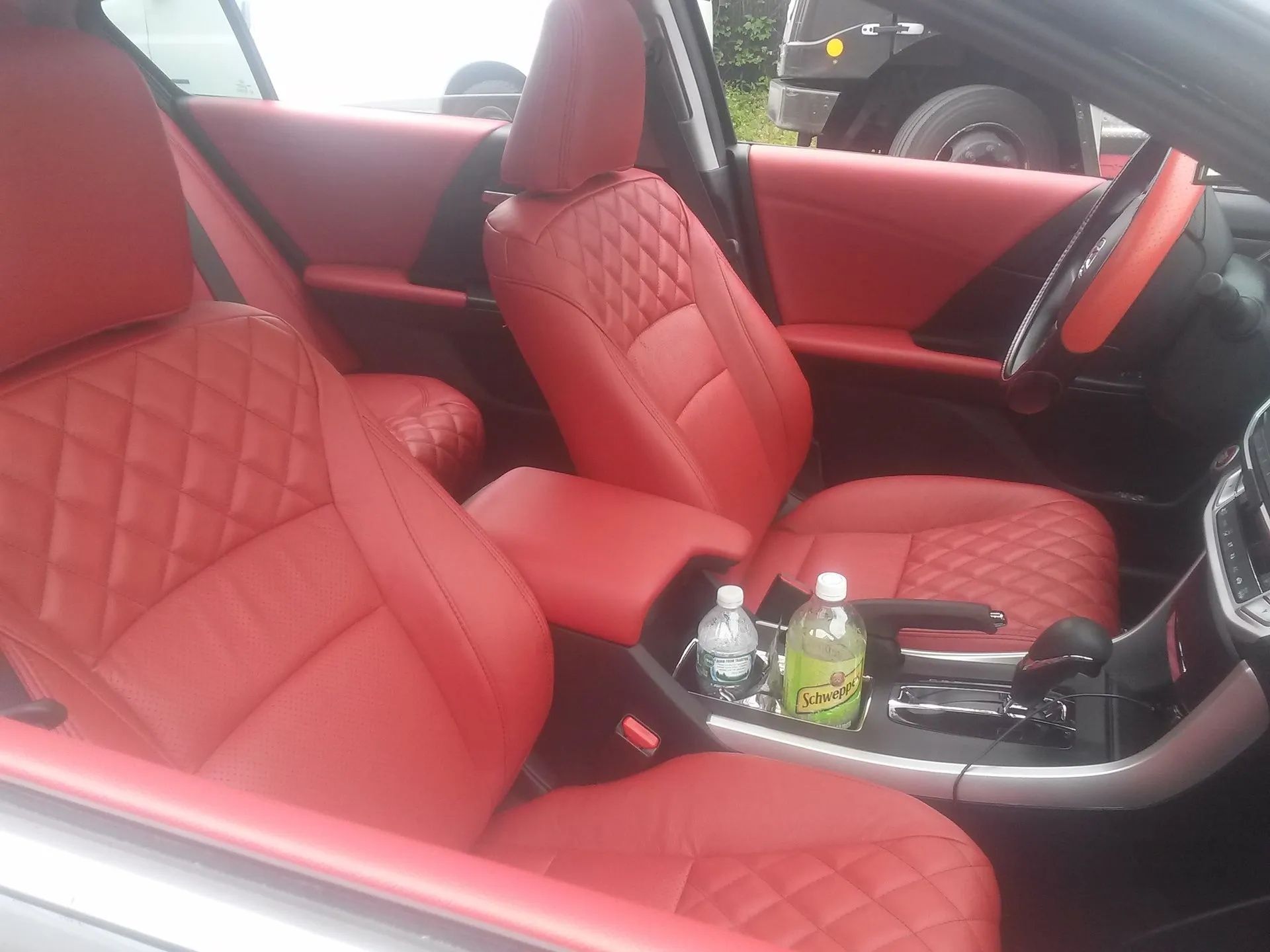 Red quilted leather car interior with seats, center console, and a bottle in the cup holder
