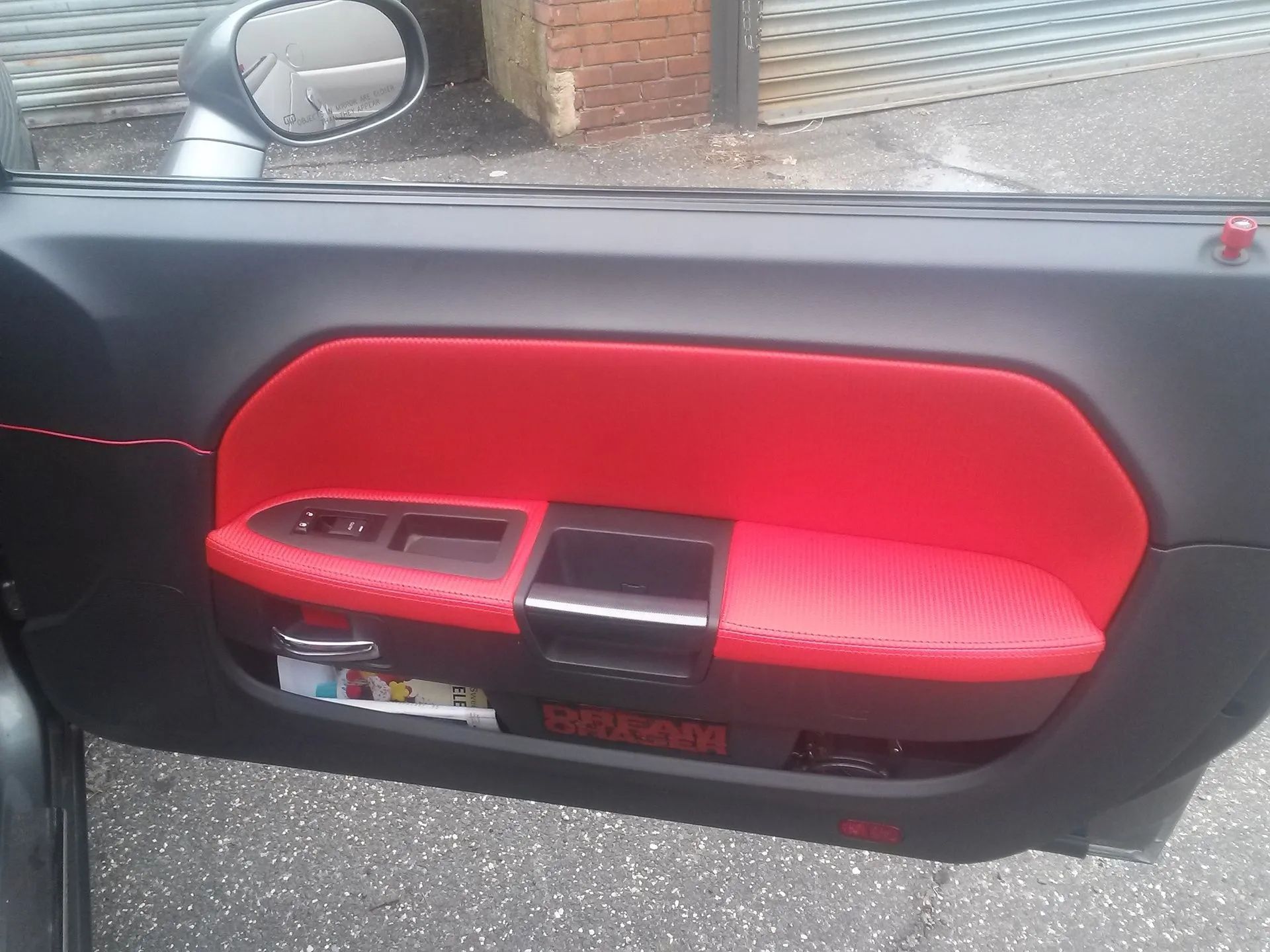 Car door interior with red and black panel, window controls, and storage pocket open to the outside.
