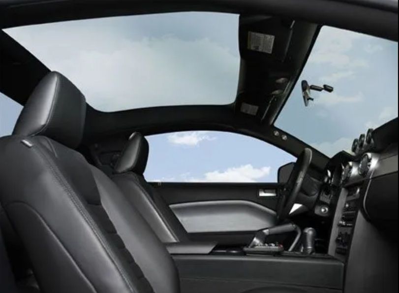 Modern car interior with black leather seats and a panoramic glass roof, viewed from the passenger side