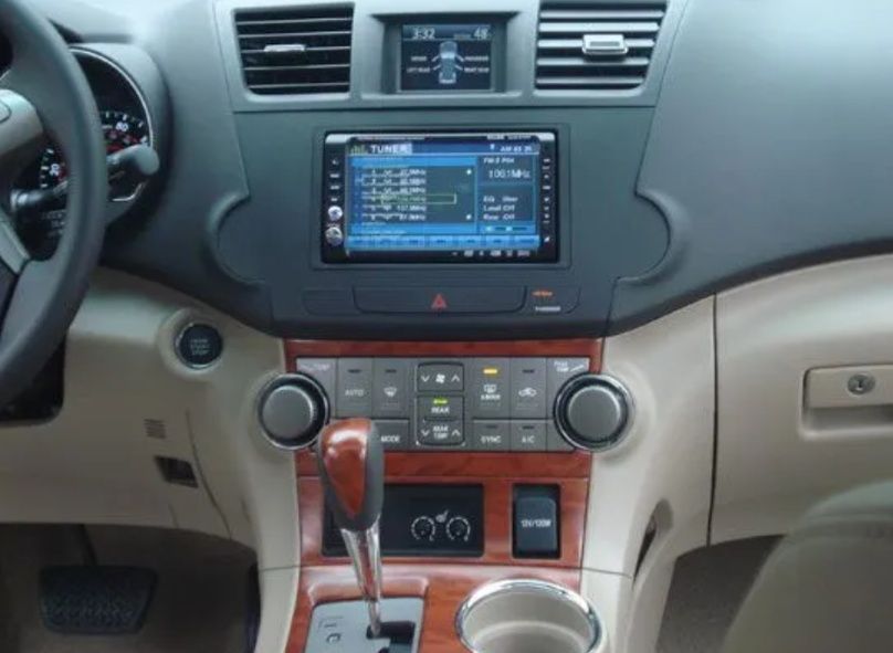 Car dashboard with a center touchscreen, climate controls, and wood trim around the gear shift.