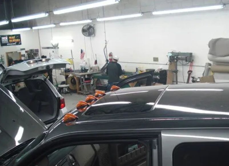 Auto repair shop with a person working at a cluttered workbench beside parked cars.