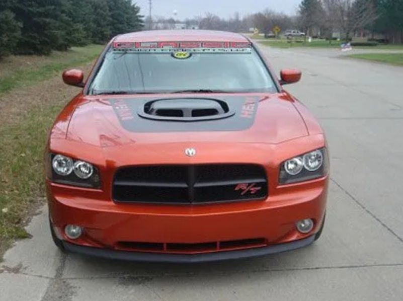 Front view of an orange Dodge Charger parked on a road with trees in the background
