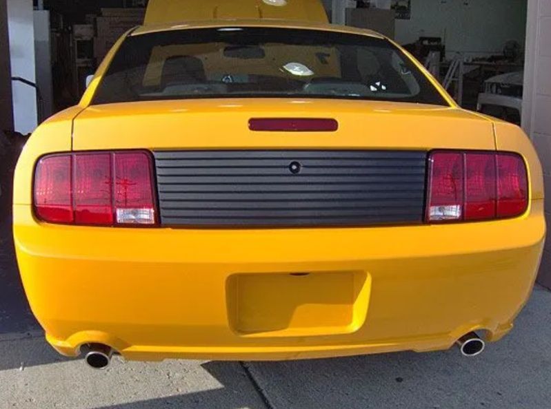 Rear view of a yellow sports car with black tail panel and red taillights in a garage