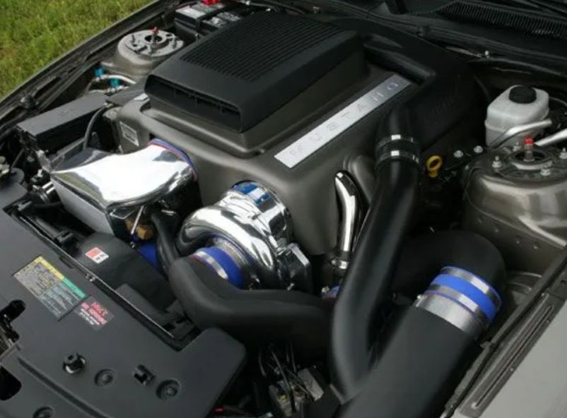 Close-up of a car engine bay with chrome and blue aftermarket performance parts and black intake piping