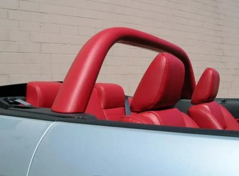 Red leather seats and roll bar in a convertible against a beige wall.