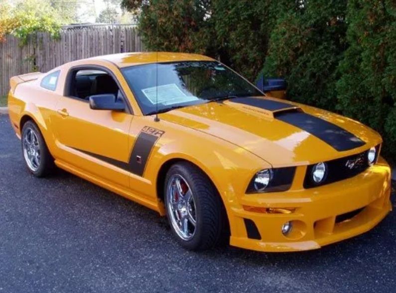 Yellow sports car parked on a street, front view with black hood accents and chrome wheels