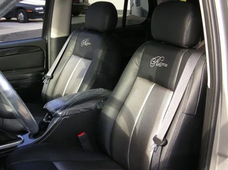Black leather car seats with gray inserts and embroidered logos inside a vehicle