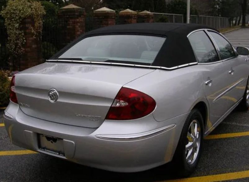 Silver sedan parked in a lot, rear view with black soft top roof