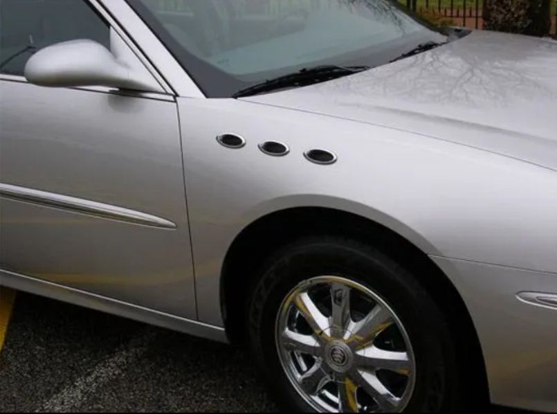 Silver sports car close-up with chrome wheel and three side vents on the front fender