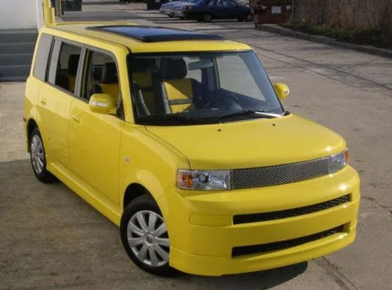 Yellow compact car parked outdoors on pavement, viewed from the front-left side.