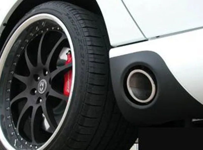 Close-up of a silver sports car’s rear wheel with black rim and red brake caliper near an exhaust pipe
