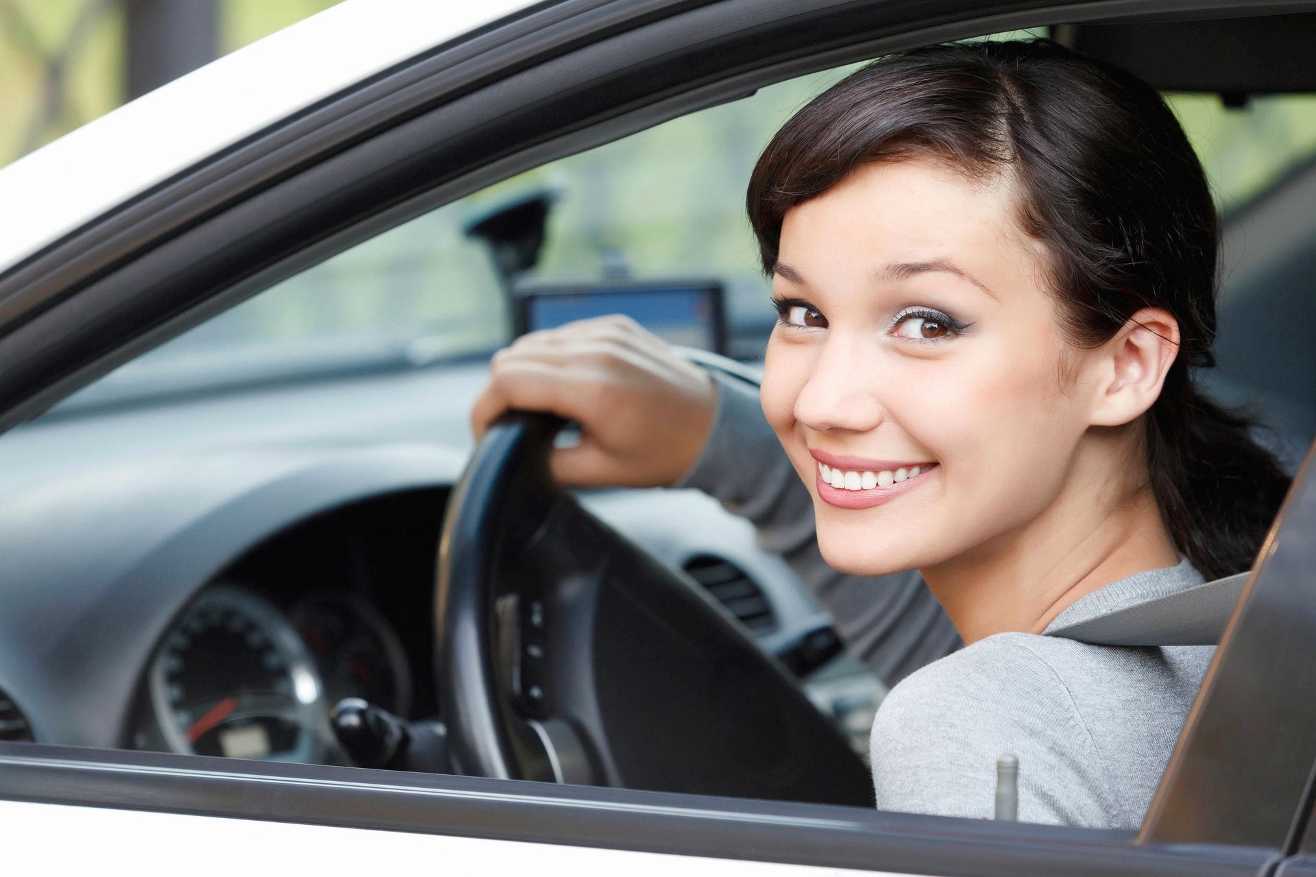 Woman smiling in white car, holding steering wheel.