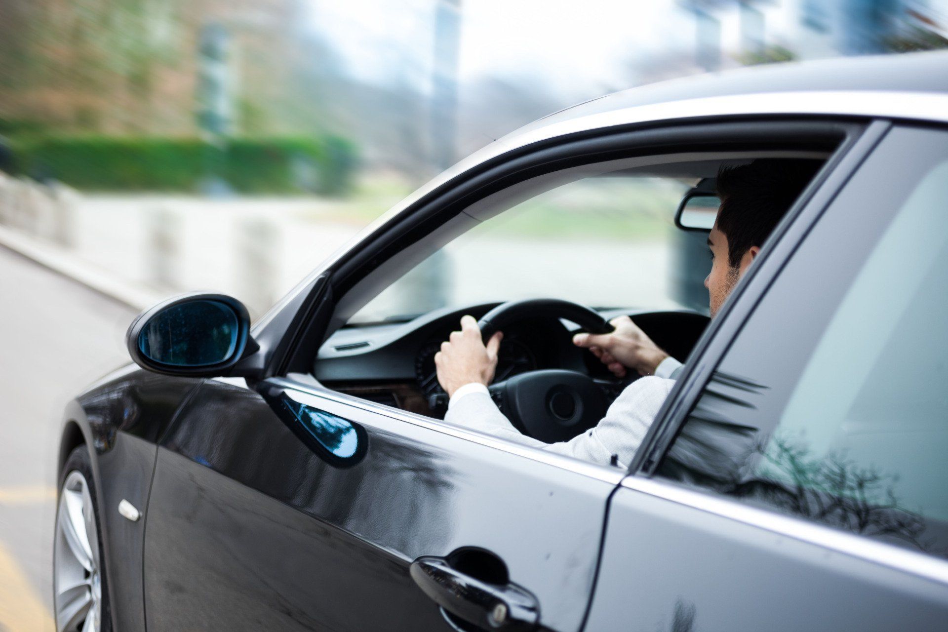 Man driving a black car, holding the steering wheel. View is from the side, focused on the driver and car's interior.
