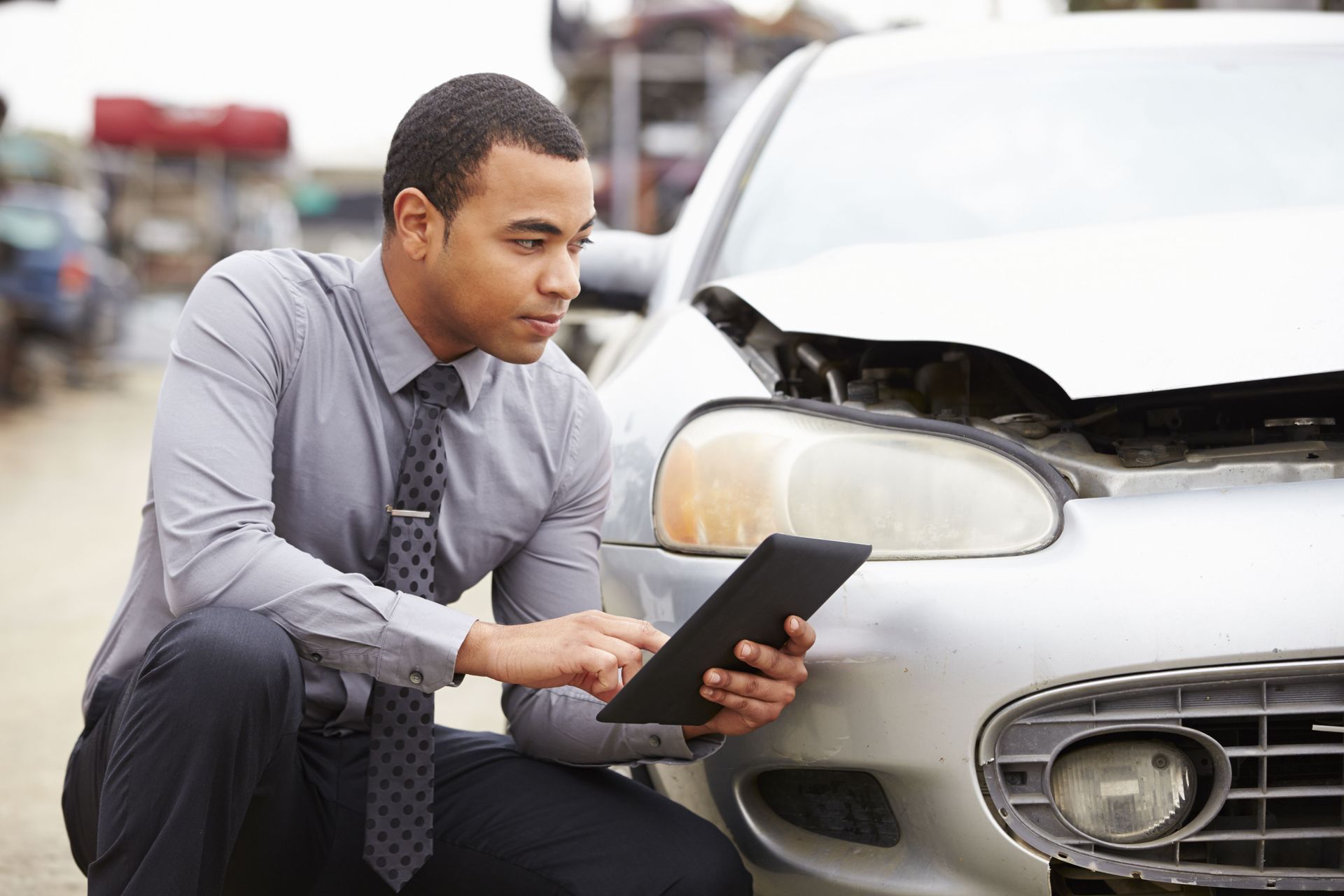 Man examining damaged car with a tablet, outdoors.