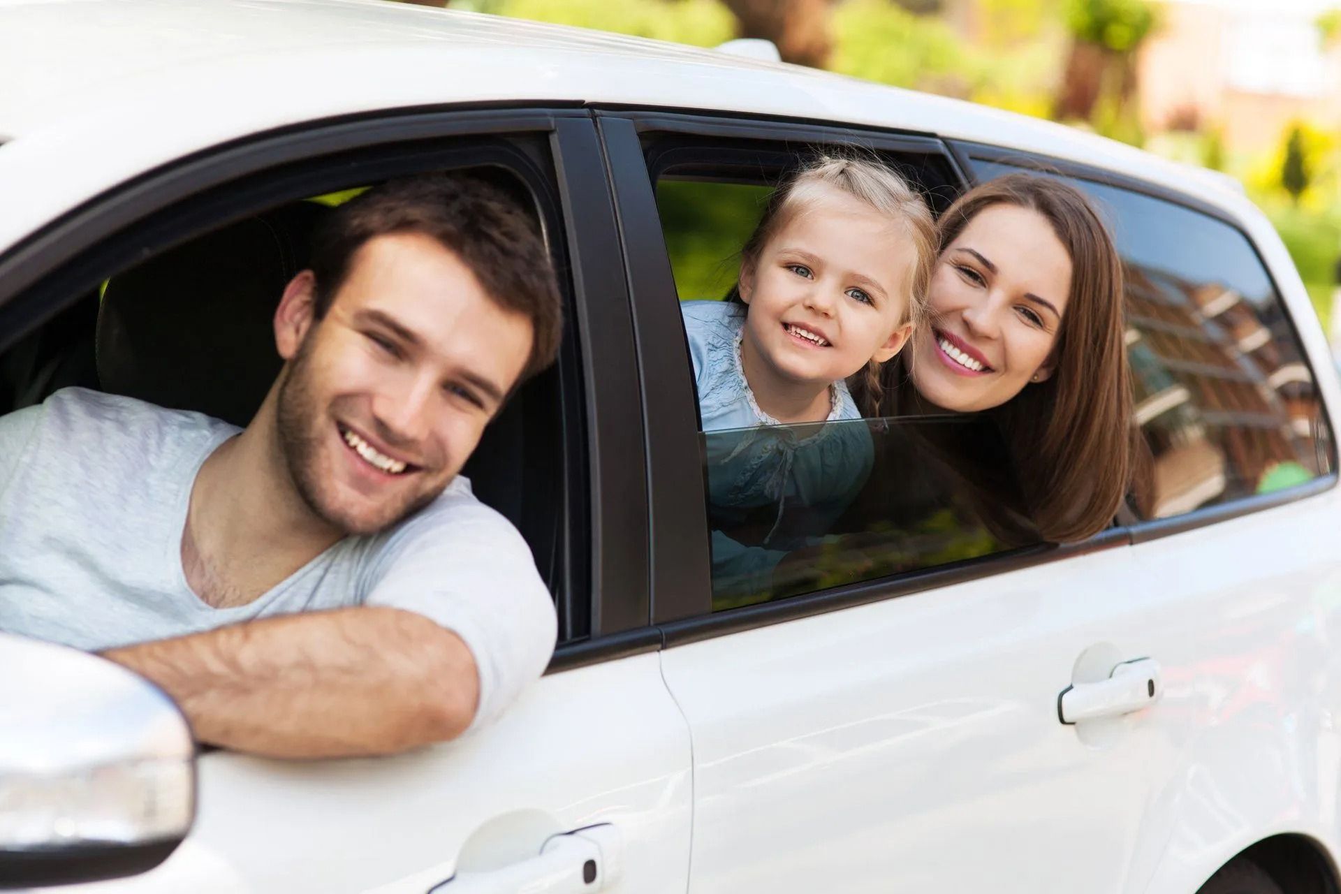 Family smiling in a white car, sunlight, happy expressions.