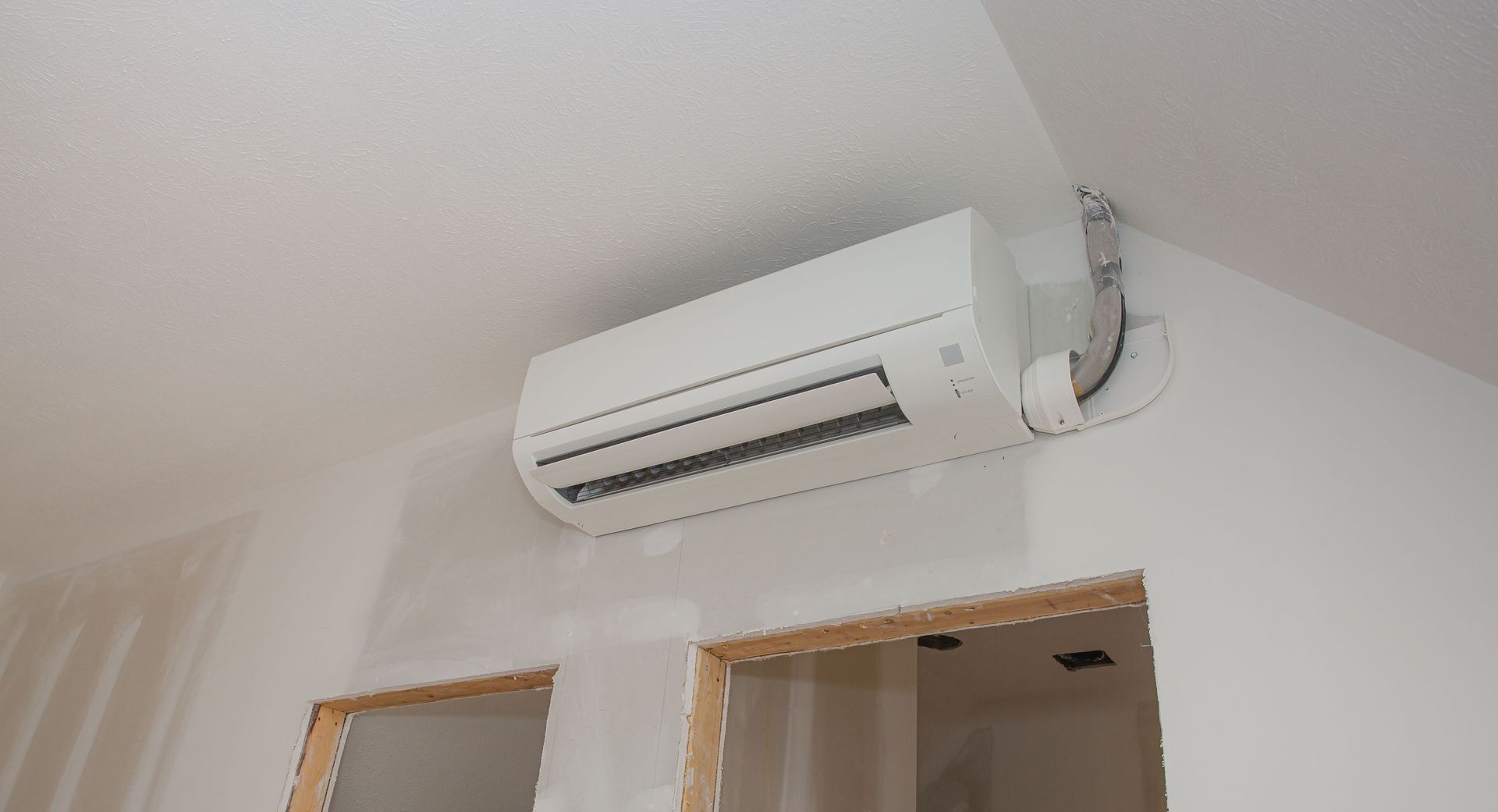White ductless air conditioning unit mounted on a white wall, above two unfinished door frames.