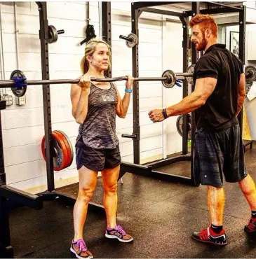 A man is helping a woman lift a barbell in a gym