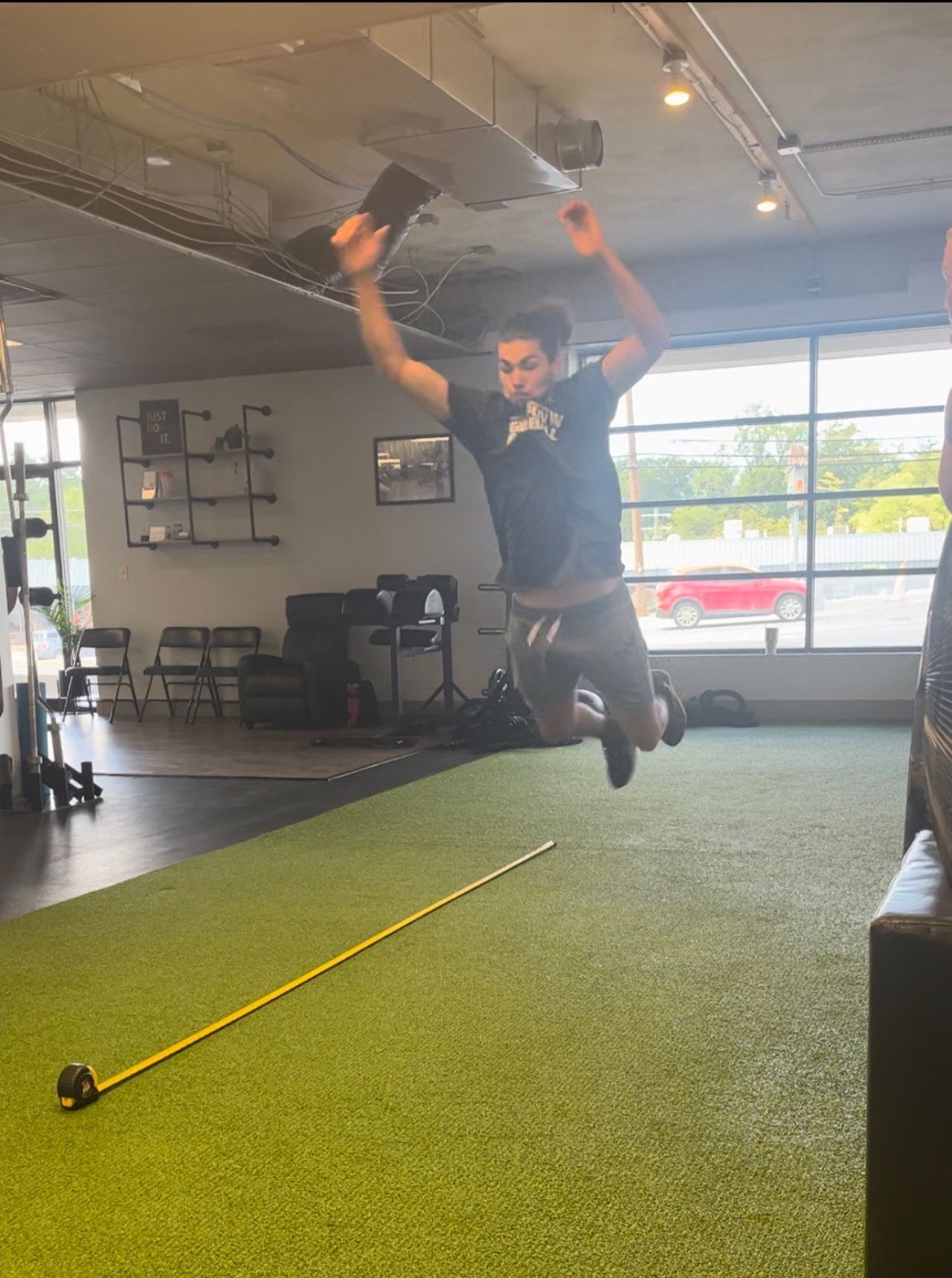 A man is jumping in the air in a gym next to a tape measure.