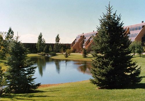 a lake surrounded by trees and grass with a building in the background