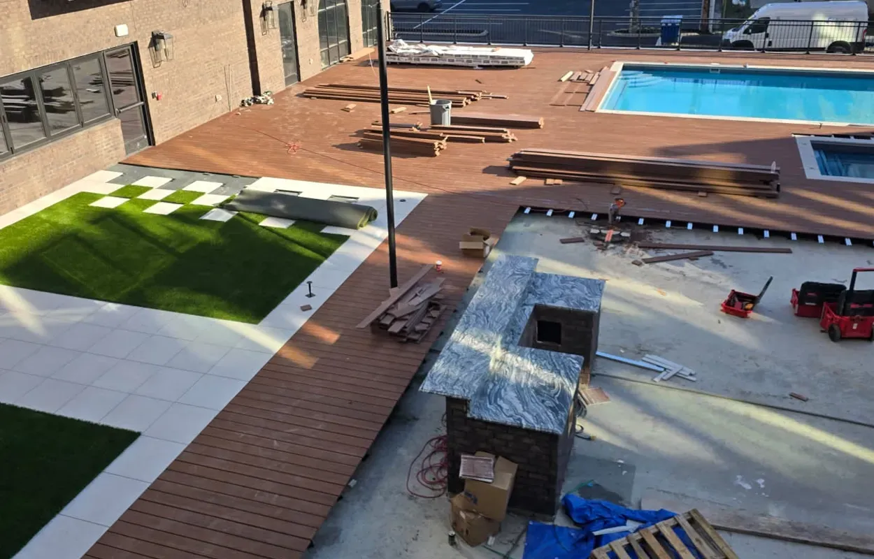 Courtyard with brick paths, green lawn, white seating area, and a swimming pool beside a building