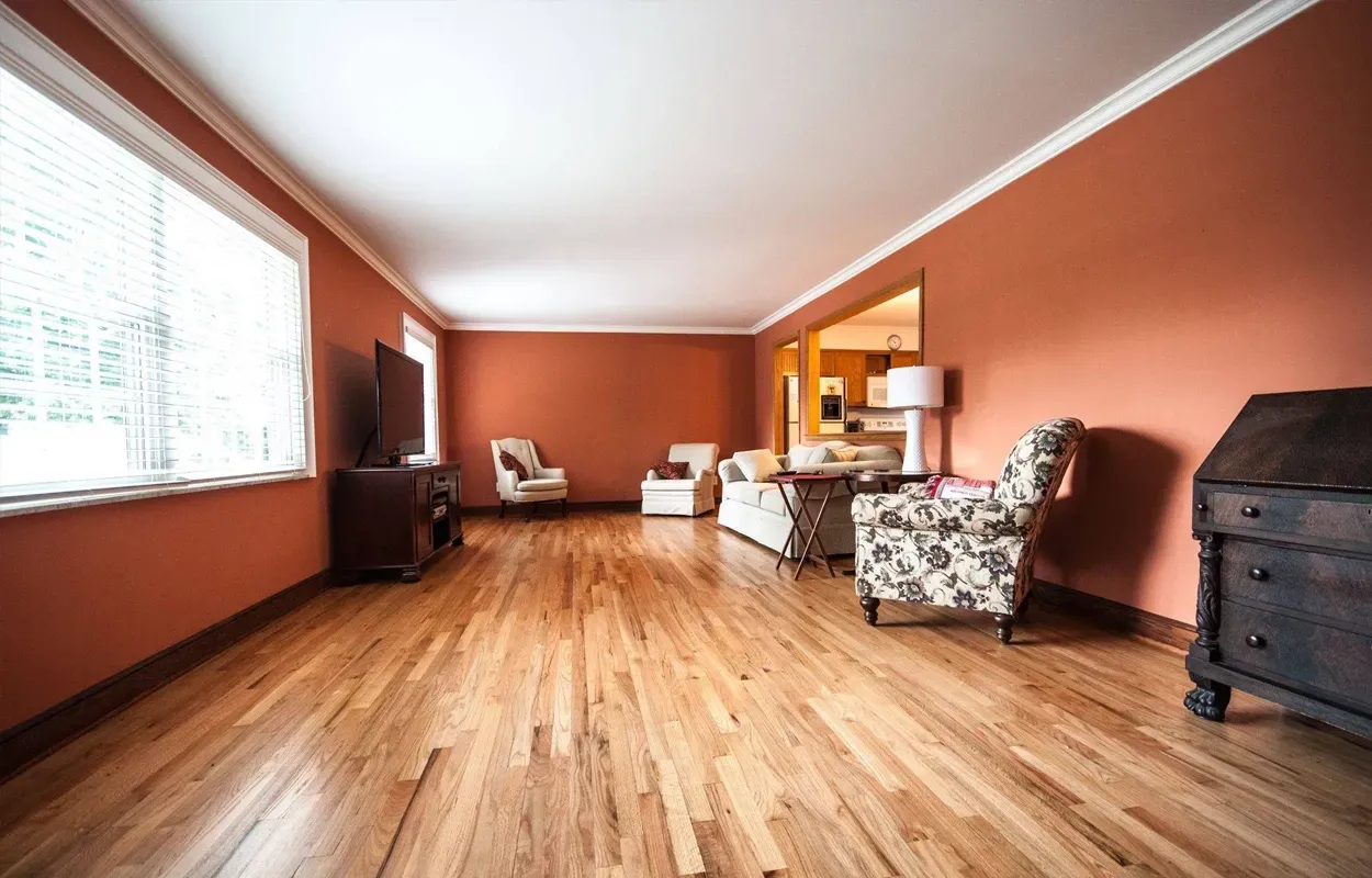 Spacious living room with orange walls, wood floors, large window, and patterned armchairs.