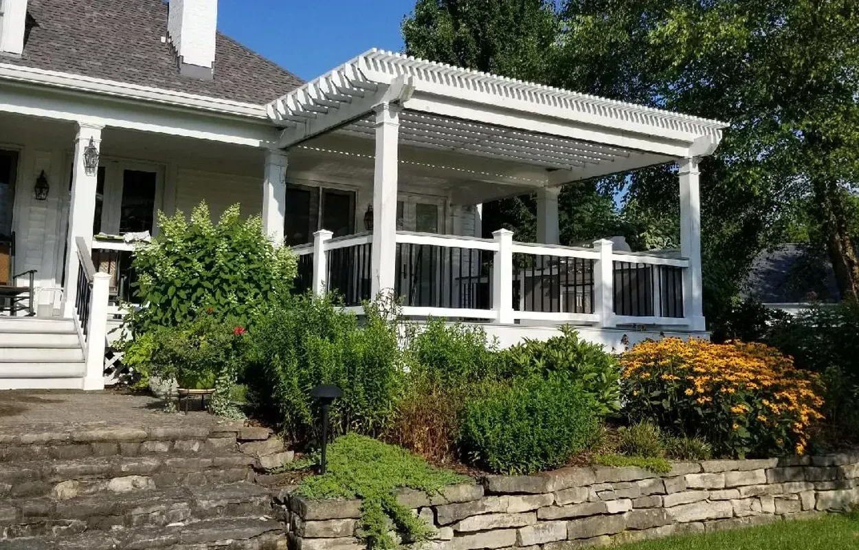 White house porch with steps, stone retaining wall, and green shrubs in the front yard.