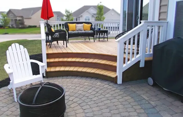 Backyard patio with curved steps, white chairs, black bench, yellow cushions, and a red umbrella