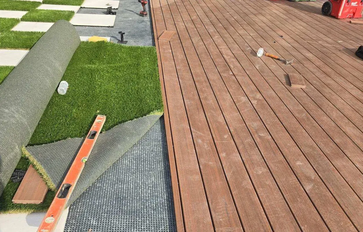 Roof repair site with orange safety straps, tools, and a person on a brown shingled roof beside green turf