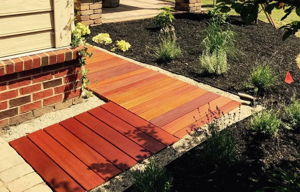 Red wooden ramp leading from a brick porch into a garden bed area.