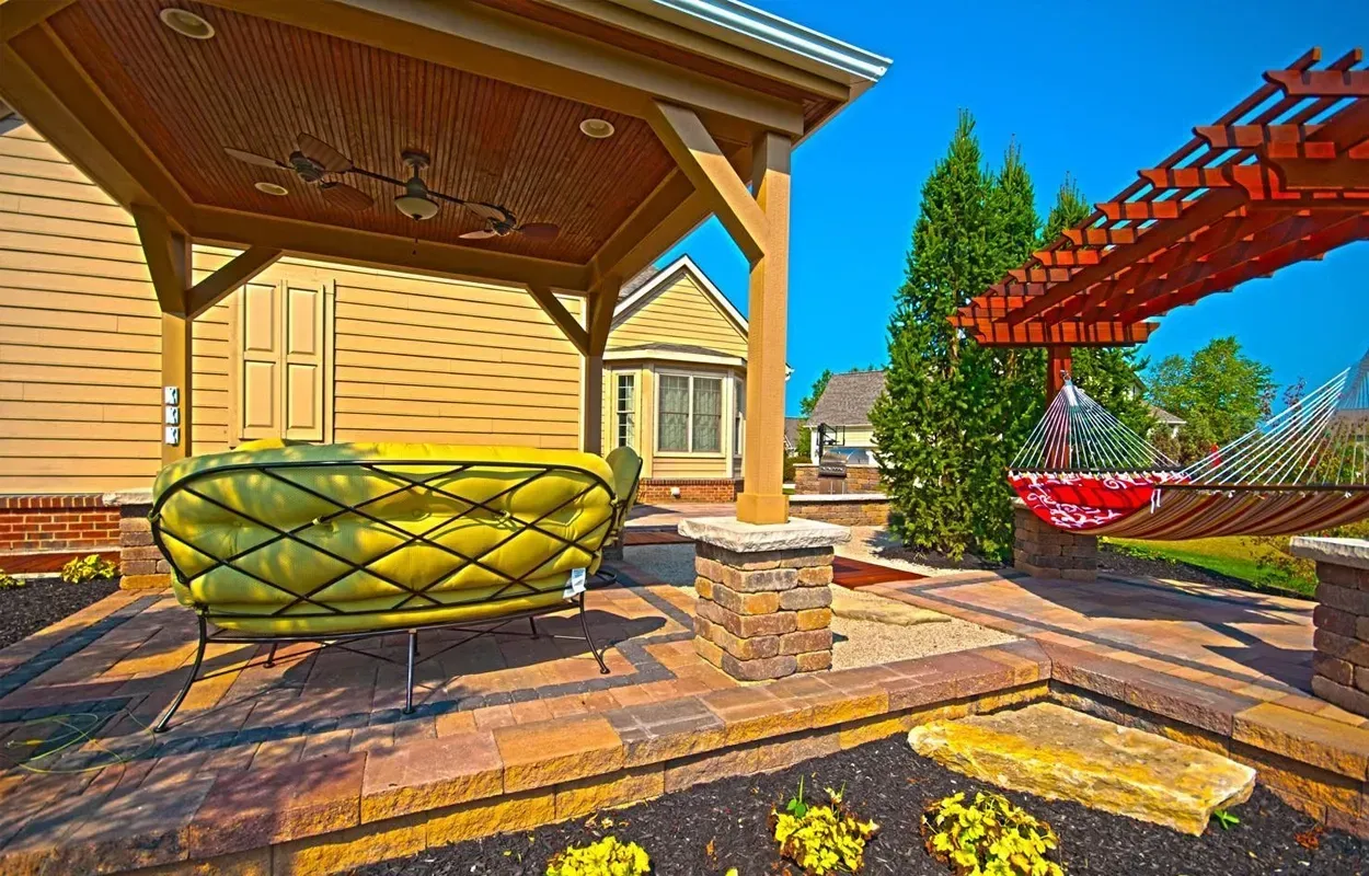 Covered patio with yellow bench, brick steps, and red pergola in a sunny backyard