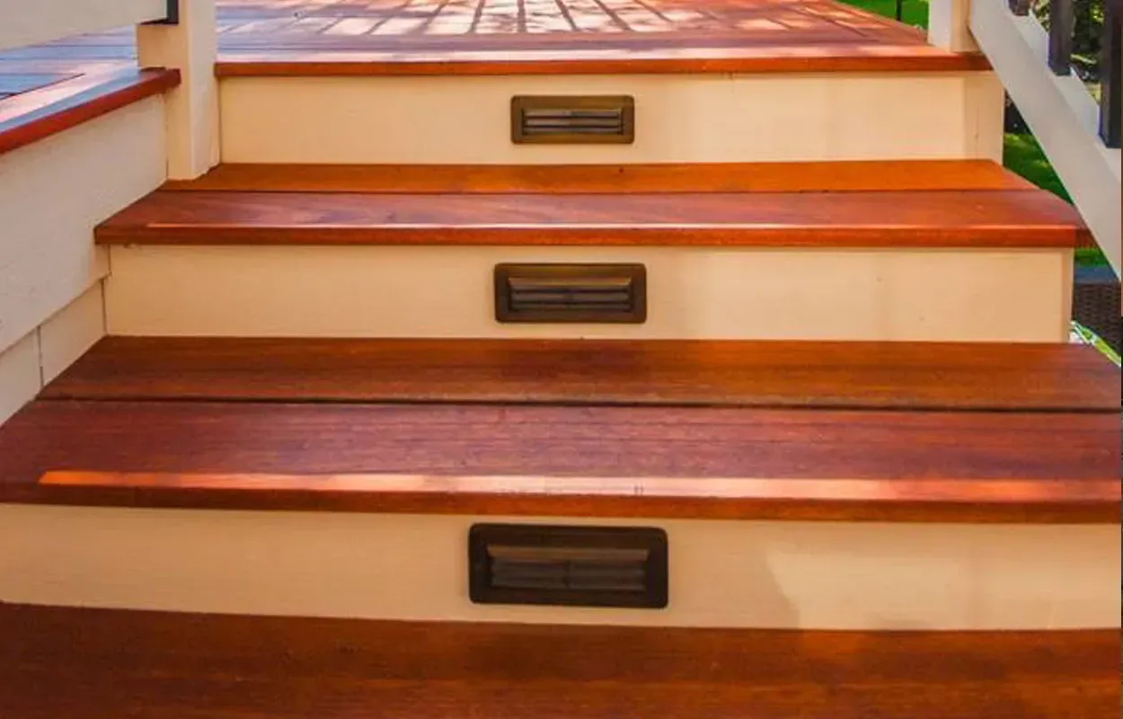 Wooden staircase with beige risers, dark treads, and rectangular vents on each step.