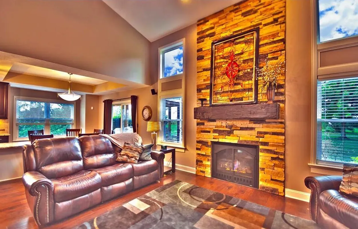 Bright living room with leather sofas, stone fireplace, wood-paneled wall, and large windows