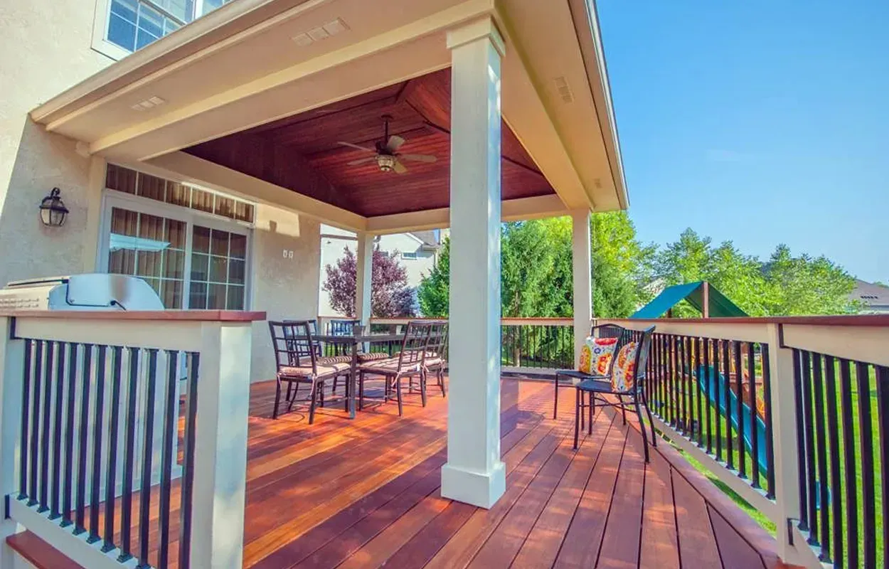 Covered wooden deck with black railings, dining table, and ceiling fan overlooking a green yard
